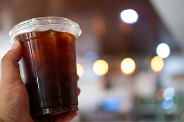 Hand holding a take away plastic cup of Iced black coffee with copy space.