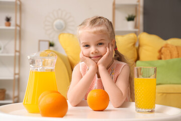 Cute little girl with orange juice and fruits near table at home