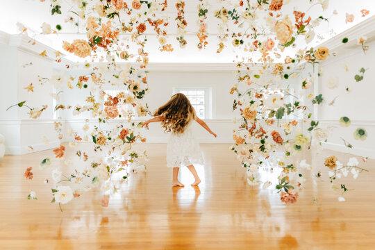 Blonde girl dances joyfully among hanging flowers in a bright room