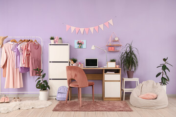 Interior of stylish teenager's room with workplace, plants and clothes rack