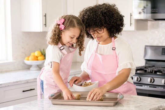 Sisters placing cookie dough on a cooking sheet in the kitchen