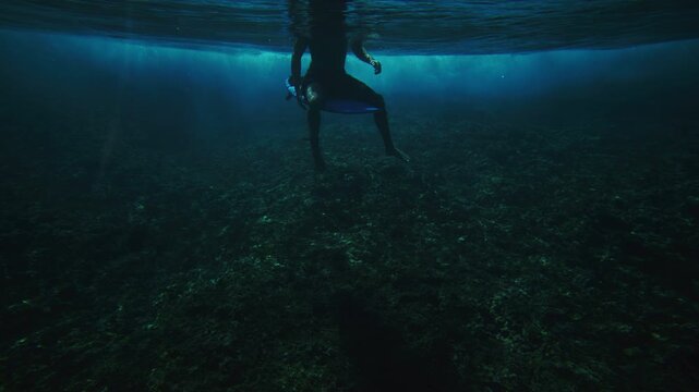 Surfer sits on shortboard straddling with legs balancing as wave crashes into whitewash behind