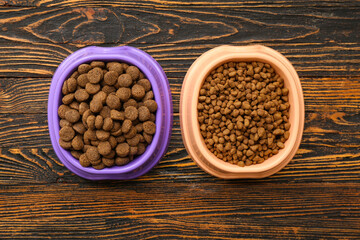 Bowls with different dry pet food on brown wooden background