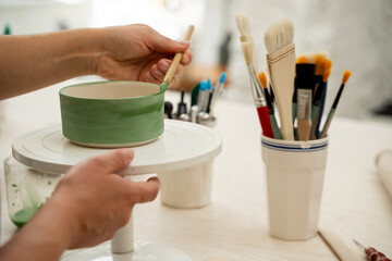 Girl is decorating a clay product with bright green color. Using a brush to paint a ceramics bowl. Learning how to paint a handmade pottery project.