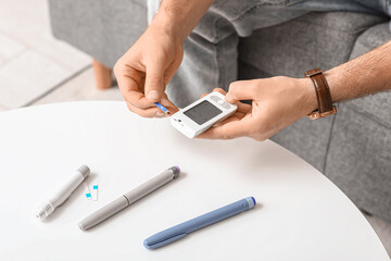 Diabetic young man using glucometer at home, closeup