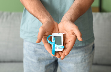 Diabetic young man with blue awareness ribbon and glucometer at home, closeup