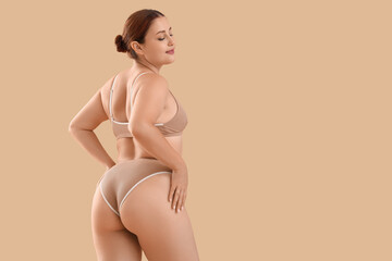 Beautiful plus size woman in underwear on beige background, back view
