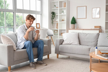 Young man with tweezers taking contact lenses on sofa at home