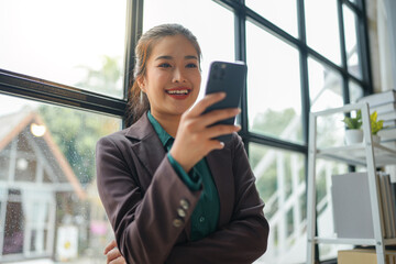 Obraz premium Asian businesswoman smiling confidently, successful entrepreneur Elegant professional company executive standing holding mobile phone in modern office working lifestyle concept.