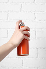 Woman with can of spray paint near white brick wall, closeup
