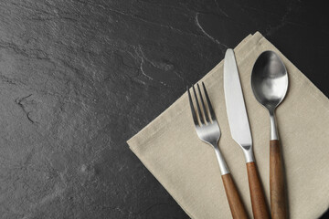 Stylish cutlery and napkin on black table, top view. Space for text