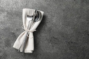 Stylish silver cutlery and napkin on grey table, top view. Space for text