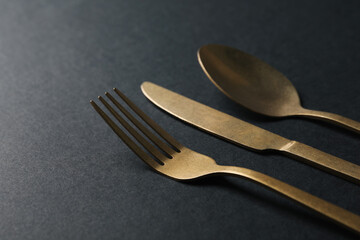Elegant golden cutlery on black background, closeup