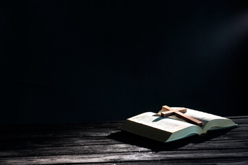 Bible and cross on black wooden table against dark background, space for text. Religion of...