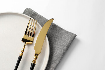 Stylish golden cutlery, plate and napkin on white background, top view. Space for text