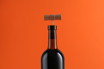 Wine bottle with corkscrew on orange background