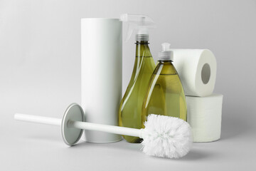 Toilet brush, holder, paper rolls and bottles of cleaning products on white background