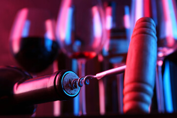 Wine bottle with corkscrew in lights on blurred background, closeup