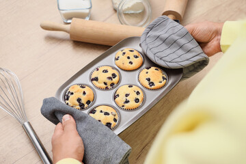 Young man putting baking dish with tasty muffins on table in kitchen, closeup