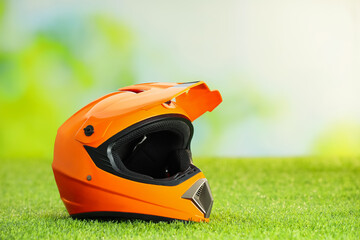 Orange motorcycle helmet with visor on green grass, space for text