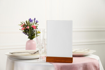 Menu holder, clean dishware and vase with beautiful flowers on white table in restaurant