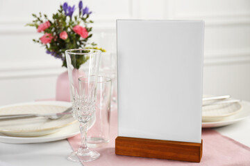 Menu holder, clean dishware and vase with beautiful flowers on white table in restaurant, closeup