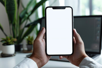 Modern office workspace with hand holding smartphone, laptop, and indoor plant