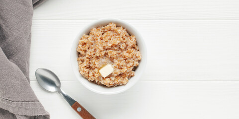 Wheat porridge with butter in a ceramic bowl on white wooden table. Healthy breakfast. Top view
