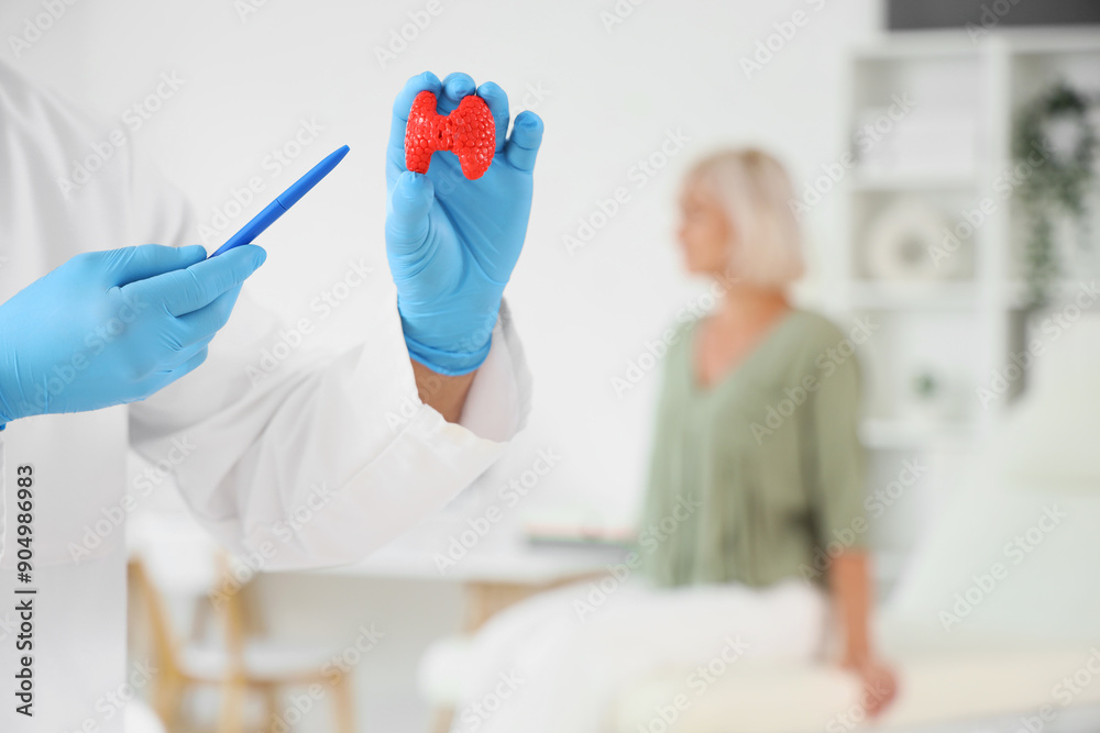 Poster male endocrinologist with thyroid gland model in clinic, closeup