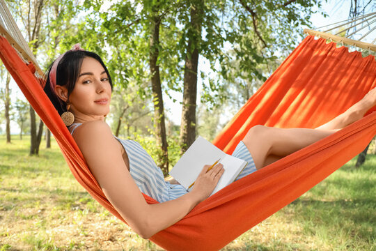 Young woman writing on notebook in hammock outdoors - Powered by Adobe