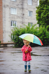 Obraz premium A little beautiful girl blonde, in boots and with umbrella walking along the puddles in the rain. Happy child. A walk under the summers of the rain.