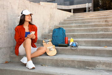 Young Asian woman in headphones with spray paint cans using mobile phone on stairs outdoors