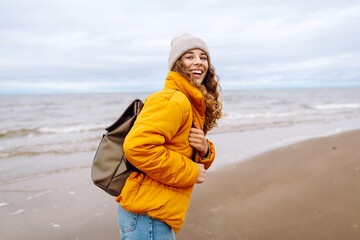 Young woman tourist walking beach on cloudy day. Stylish woman going coastline contemplating life on cold weather.  Active lifestyle.