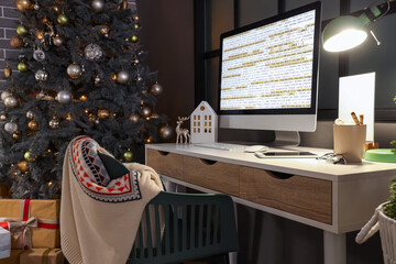 Programmer's workplace with computer and cocoa in dark office decorated for Christmas