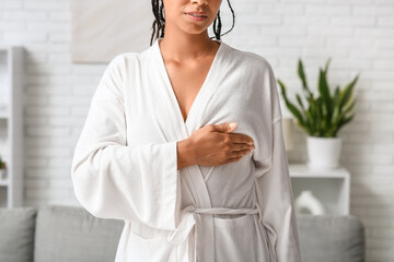 Young woman in bathrobe checking her breast at home. Cancer awareness concept