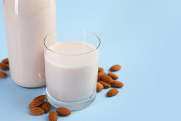 Fresh almond milk in glass, bottle and nuts on light blue background, space for text