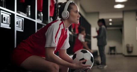 Girl, soccer and headphones with ball in locker room for preparation or getting ready with team for game. Female person or sports player with earphones and waiting in half time for next match or play - Powered by Adobe
