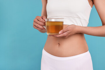 Weight loss concept. Woman with cup of diet tea on light blue background, closeup