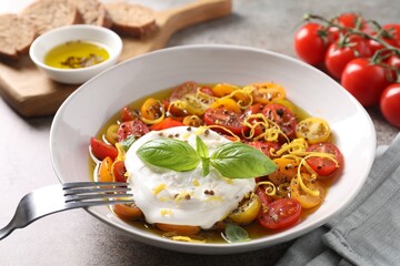 Delicious fresh burrata salad in bowl served on gray textured table, closeup