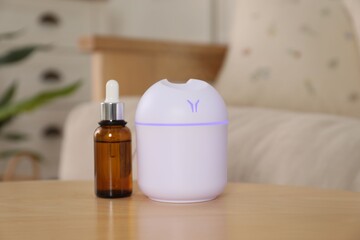 Aroma diffuser and bottle of essential oil on wooden table at home