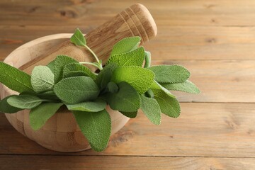 Green sage leaves and pestle in mortar on wooden table, closeup