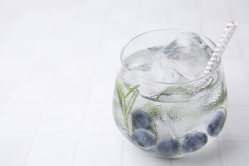 Refreshing water with blueberries and rosemary in glass on white tiled table, closeup. Space for text