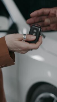 Close-up vertical slowmo of hand of anonymous dark-skinned male mechanic or salesman giving car key to female customer after purchase at dealership or maintenance in garage