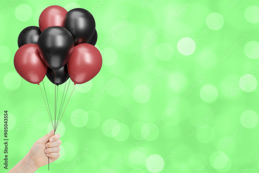 Poster child's hand holds bunch of red and black balloons on blurred summer green background. empty space f