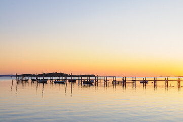 Fototapeta premium Golden hues reflect on calm waters as small boats rest beside a wooden dock, capturing the peaceful essence of twilight.