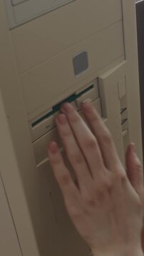 Vertical high angle shot of hands of anonymous clerical worker choosing green floppy diskette and inserting it into outdated computer while working in office in 90s