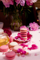 macaroni cookies on a plate, next to a teapot with tea. Pink tablecloth and flowers on the table