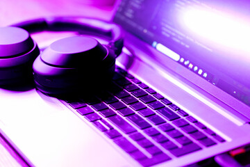 modern wireless headphones and laptop with software code on screen in neon purple light,  suitable...