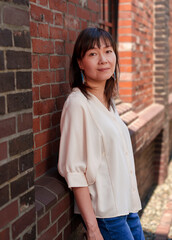 Fototapeta premium 煉瓦の壁に寄りかかってこちらを向く女性