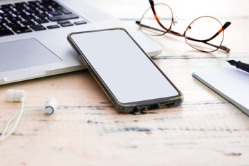 A modern wooden desk with a mobile phone displaying a map, reading glasses, headphones, a pen, and a notebook. The setup suggests navigation or research in a productive workspace.